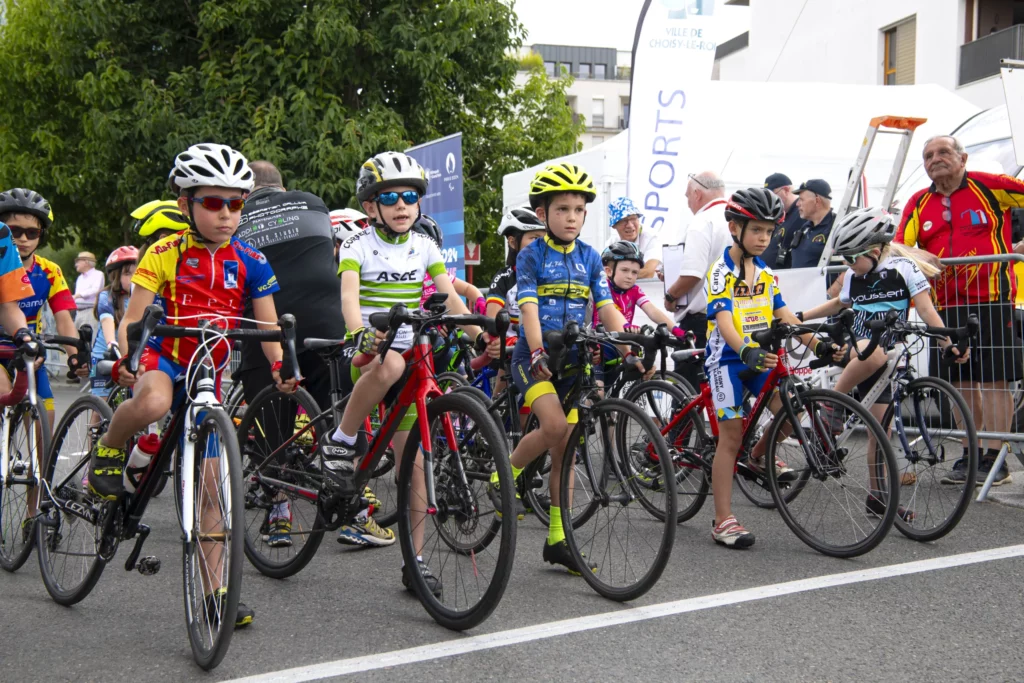 Jeunes cyclistes alignés et prêts pour le départ d'une course, portant des maillots colorés et des casques.